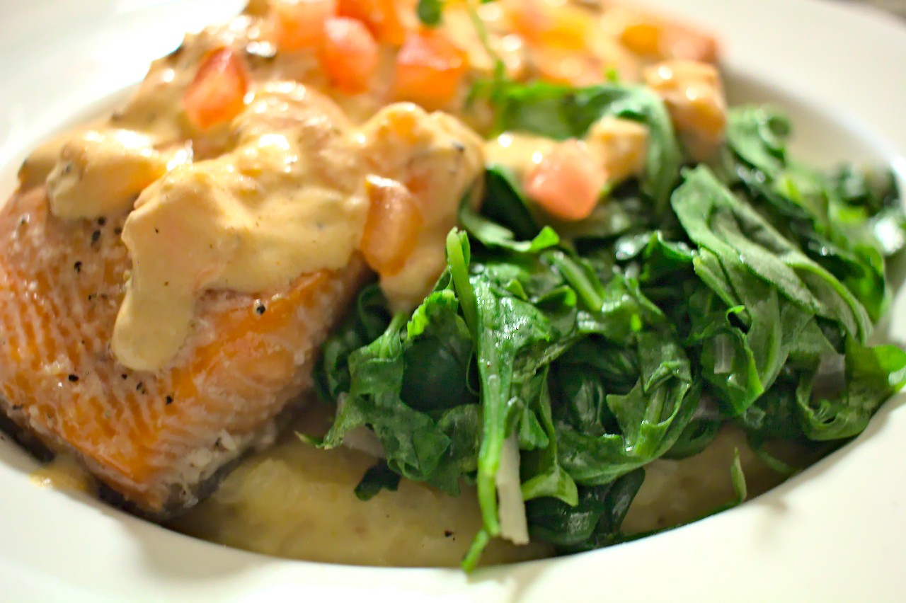 Closeup shot of oven roasted salmon next to wilted arugula on top of risotto
