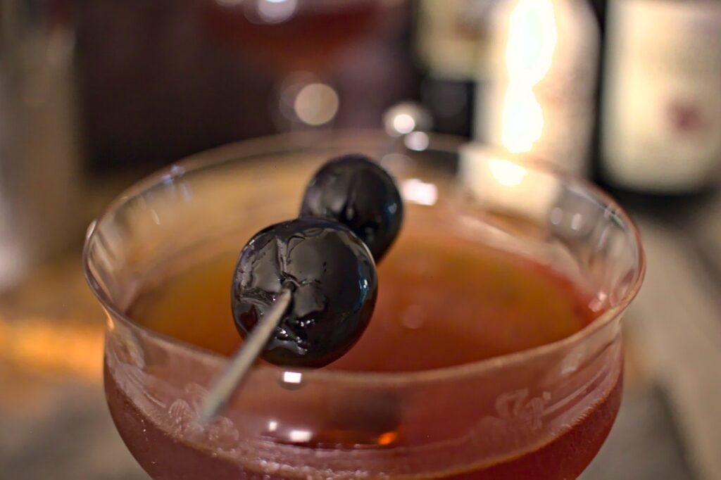 Closeup photo of tart cherry liqueur manhattan in a coupe glass garnished with maraschino cherries