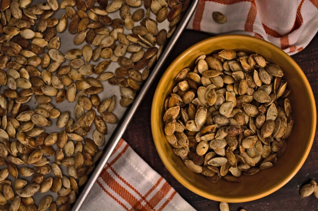 Overhead photo of roasted pumpkin seeds in a bowl and on a sheet pan