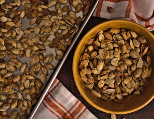 Overhead photo of roasted pumpkin seeds in a bowl and on a sheet pan